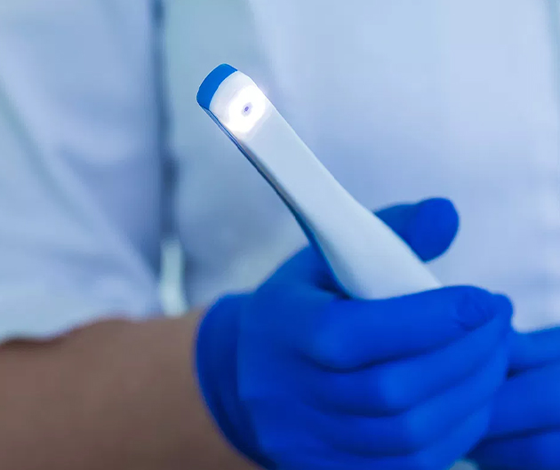 Dentist in blue gloves holding dental intraoral camera tool for examination.