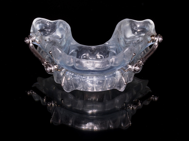 Clear dental night guard or oral appliance displayed against black background with reflection.