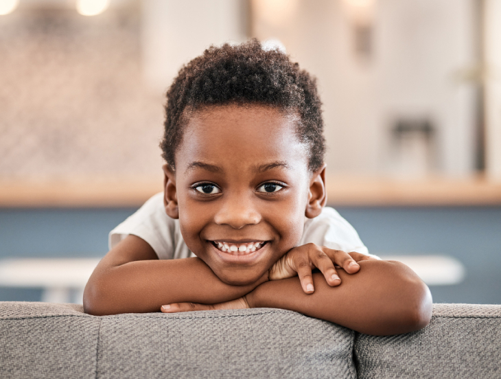 Happy young child smiling at camera, leaning on gray surface in bright dental office setting.