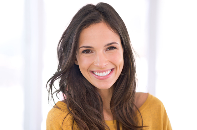 Smiling woman in yellow shirt in bright dental office setting, professional headshot.
