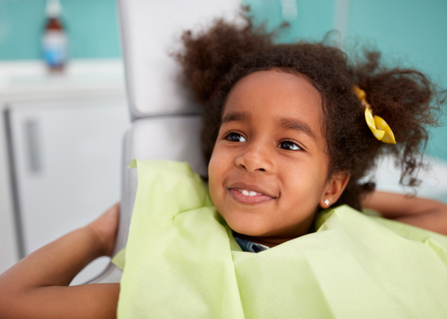 Young child in yellow shirt smiling in bright, modern dental office setting.