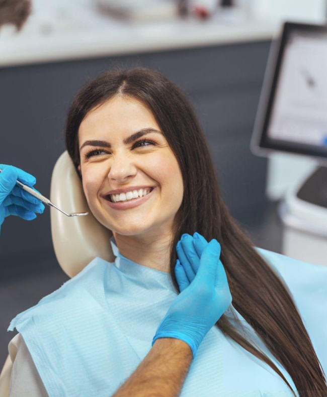 Smiling female dental professional in blue gloves and mask at dental office workstation.