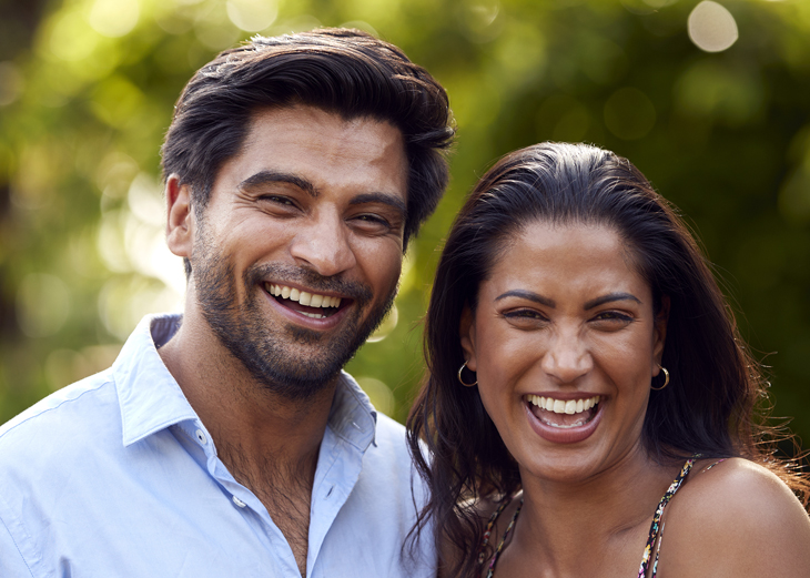 Smiling couple outdoors in natural sunlight, representing happy dental patients or family dentistry clients.