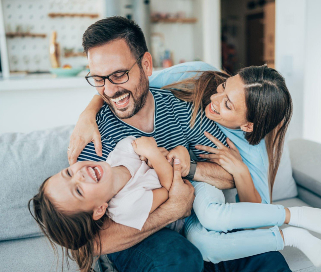 Happy father playing with two young children on couch at home.