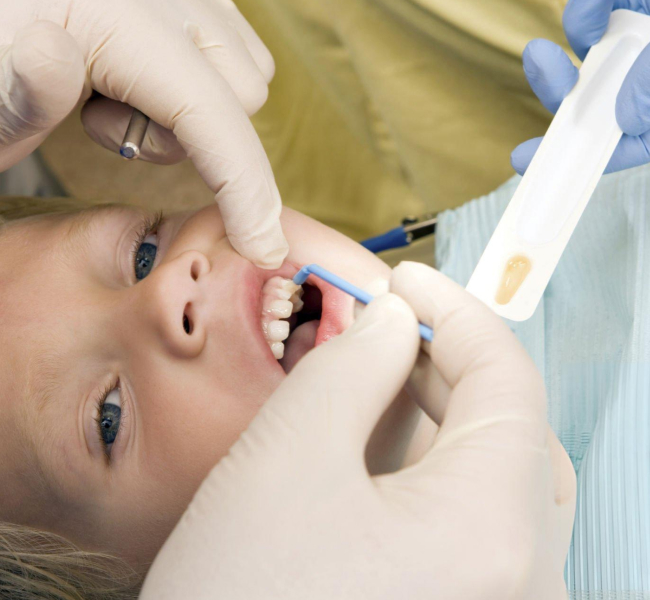 Child receiving dental examination in dentist's office with gloved professional hands.