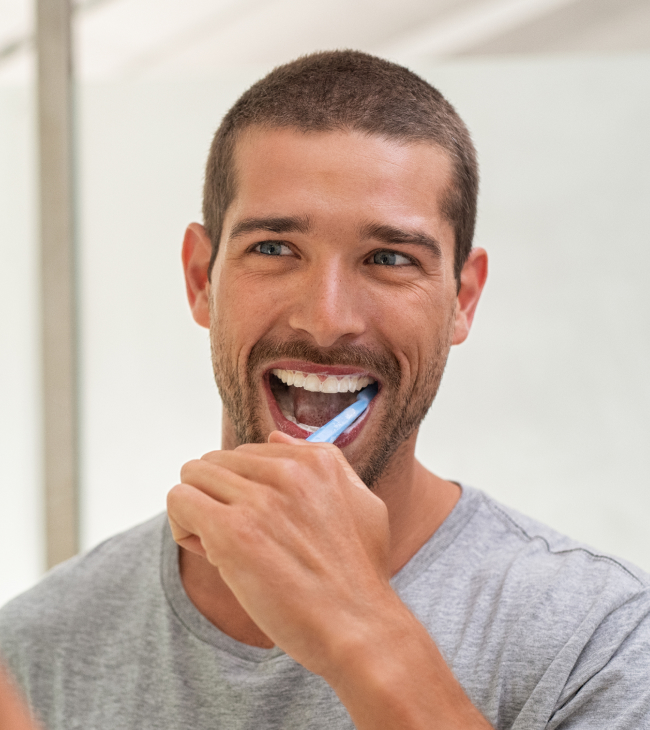 Man brushing teeth with toothbrush in bathroom, smiling at camera.