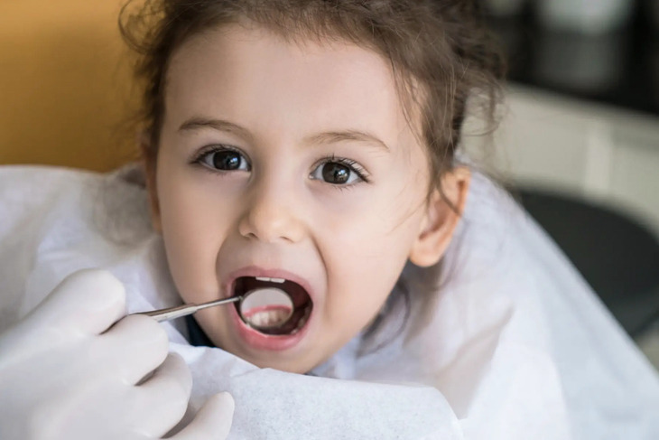 Young child at dental visit with mouth open during examination by dentist.