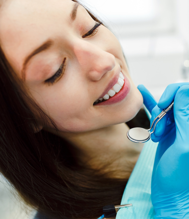 Woman receiving dental examination from dentist wearing blue gloves in clinical setting.