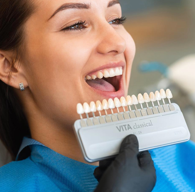 Woman smiling while holding dental shade guide for teeth whitening consultation at dentistry office.
