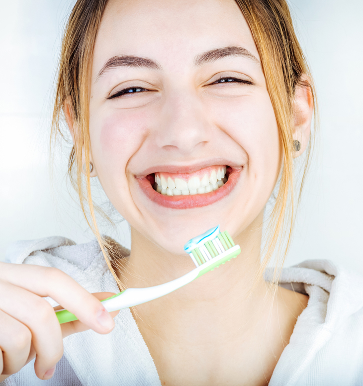 Young woman smiling while holding toothbrush with toothpaste, promoting dental hygiene.