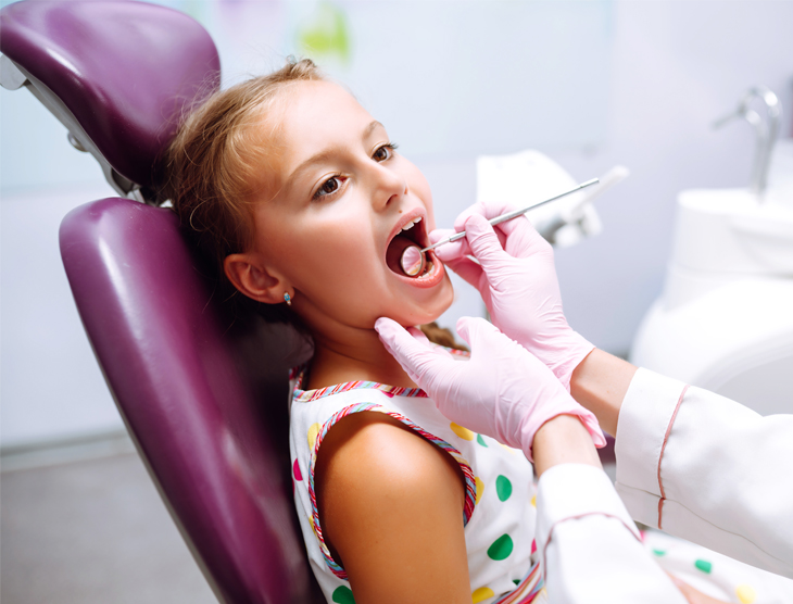 Young girl receiving dental examination in dentist chair with gloved dentist.