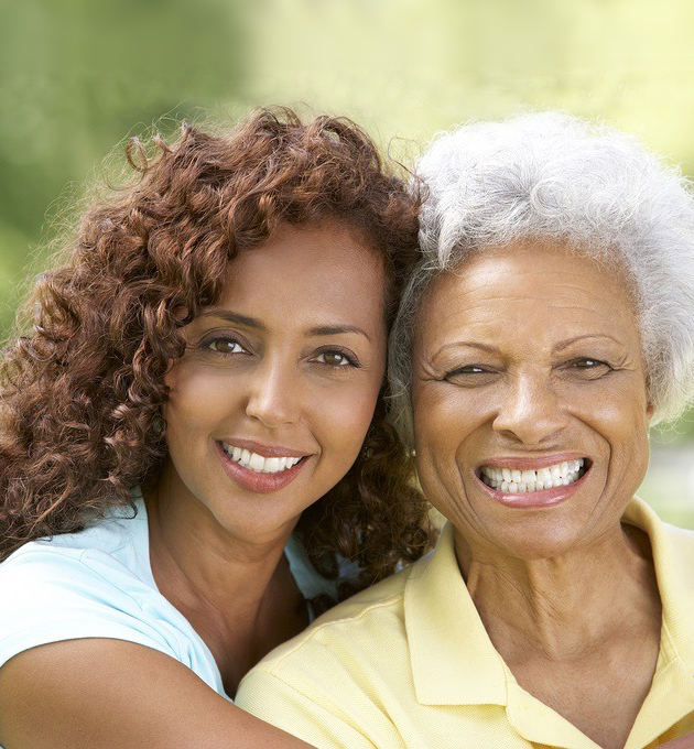 Two women smiling together outdoors in natural daylight, representing family dentistry care and relationships.