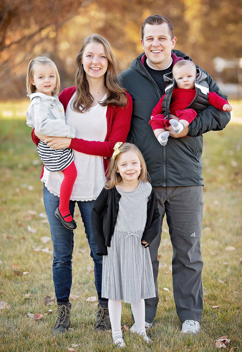 Happy family of five smiling outdoors in fall setting wearing coordinated red and neutral clothing.