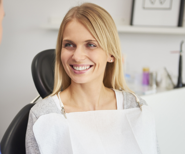 Smiling female dentist in white coat at dental office desk.