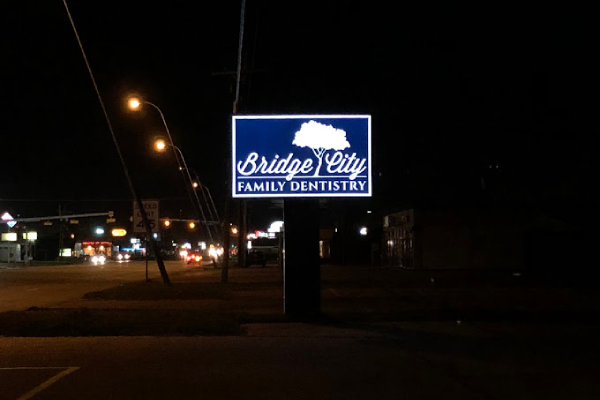Illuminated Bridge City Family Dentistry sign at night on roadside storefront.